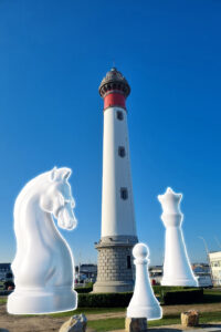 Montage photo du phare de Ouistreham entouré de pièces d'échecs géantes
