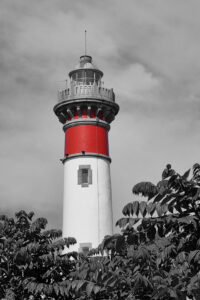 Photo noir et blanc du phare de Ouistreham dont la seule couleur présente est le rouge.