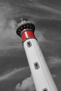 Photo noir et blanc du phare de Ouistreham dont la seule couleur présente est le rouge.