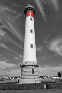 Photo noir et blanc du phare de Ouistreham dont la seule couleur présente est le rouge.