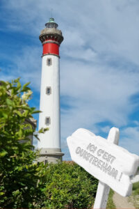 Montage photo du phare de Ouistreham vers lequel pointe une pancarte "Ici c'est Ouistreham !"